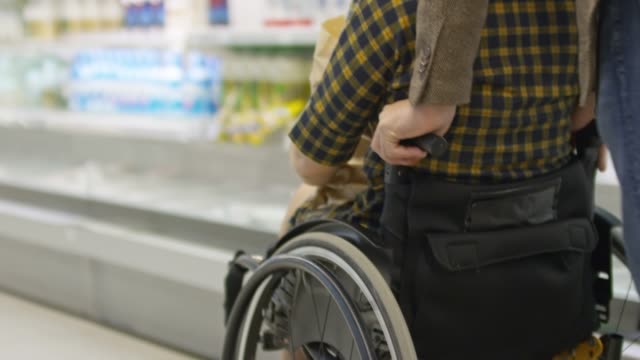Hombre-empuja-a-mujer-con-discapacidad-en-silla-de-ruedas-en-la-tienda-de-comestibles