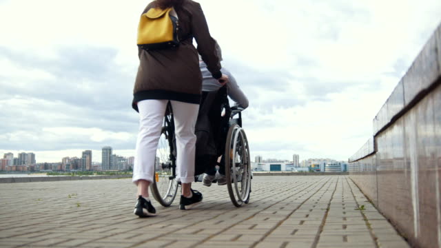 Woman-carries-a-disabled-man-in-a-wheelchair-walking-down-the-street