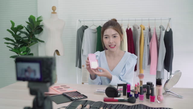 Beauty-blogger-present-beauty-cosmetics-sitting-in-front-camera-for-recording-video.-Beautiful-asian-woman-use-brush-while-review-make-up-tutorial-broadcast-live-video-to-social-network-by-internet.