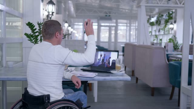 Lernenden-Behinderte-Mann-im-Rollstuhl-schreibt-Notizen-im-Notizbuch-beim-Ansehen-von-Online-Schulungen,-sitzen-an-einem-Tisch-im-restaurant