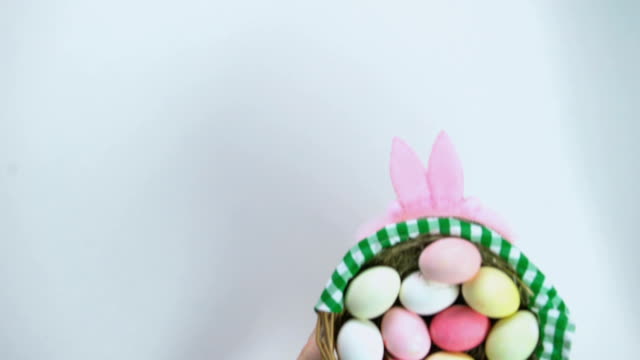 Inscripción-de-Pascua-Feliz,-mujer-manos-poniendo-la-cesta-con-los-huevos-coloreados-en-mesa