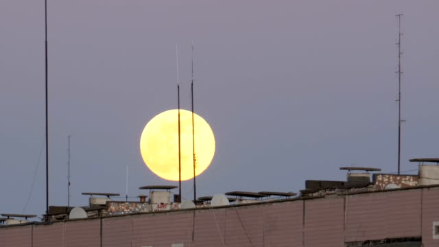 La-gran-luna-llena-sobre-el-tejado-de-un-edificio-Multistory-se-está-moviendo-hacia-arriba