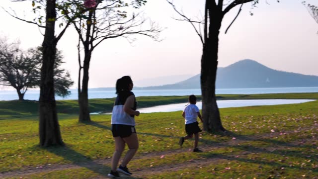 Eine-fette-asiatische-Frau-joggt-abends-in-natürlichem-Sonnenlicht,-zusammen-mit-seinem-Sohn-läuft.--Für-gute-Gesundheit.-Zeitlupe