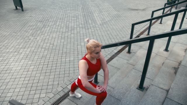 Plus-Größe-gemischte-Rasse-blonde-lächelnde-Frau-trägt-rote-Sportbekleidung-aufwärmen,-bevor-der-Lauf