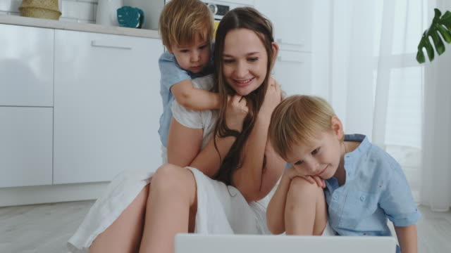 Mom-and-two-children-play-sitting-on-the-floor-hugging-and-having-fun.-A-happy-family.-The-game-after-viewing-the-laptop.-Games-with-children