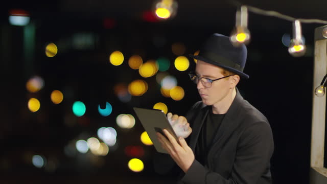 Hombre-joven-usando-la-tableta-en-la-azotea-en-la-ciudad-nocturna