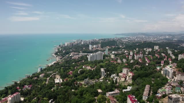 Aerial-video-shooting.-Panoramic-view-from-the-height-of-the-city-of-Sochi.-Green-trees-and-mountains-by-the-sea.-Residential-area.-Tall-houses-on-the-beach.-Blue-and-clear-sky.