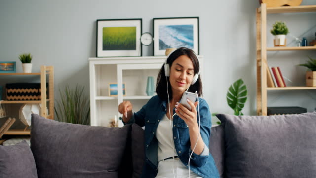 Happy-relaxed-girl-listening-to-music-in-headphones-holding-smartphone