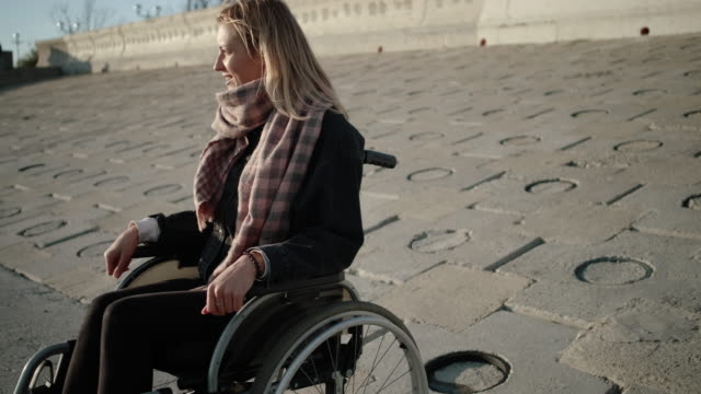 Mujer-alegre-usuario-de-silla-de-ruedas-está-sentada-en-el-terraplén-en-primavera-y-sonriendo