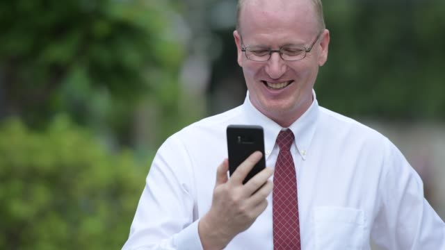 Face-of-happy-mature-bald-businessman-using-phone-outdoors