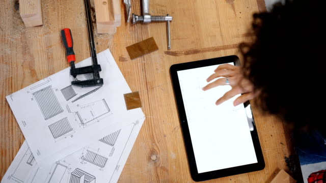 Top-view-of-female-carpenter-looking-at-technical-drawings-on-tablet-screen