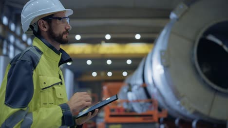 Schwerindustrie-Ingenieur-gehen-durch-Rohrherstellung-Fabrik,-verwenden-digitale-Tablet-Computer.-Anlage-für-den-Bau-von-Öl-,-Gas--und-Kraftstoffpipeline-Transportprodukten.-Seitenansicht-Zeitlupe