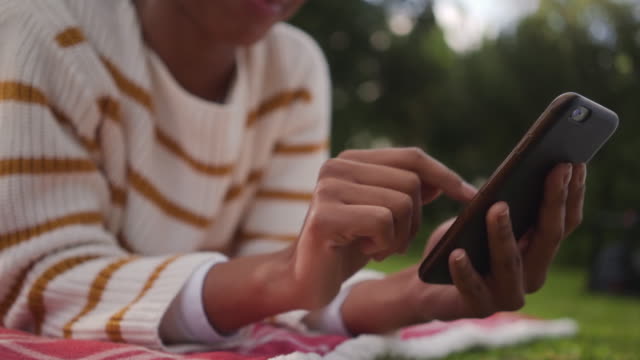 Primer-plano-de-una-joven-africana-que-yacía-en-el-parque-usando-la-aplicación-de-medios-sociales-en-el-teléfono-móvil