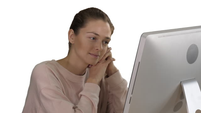 Chica-rubia-con-jersey-rosa-mirando-monitor-de-ordenador-viendo-vídeo-sobre-fondo-blanco
