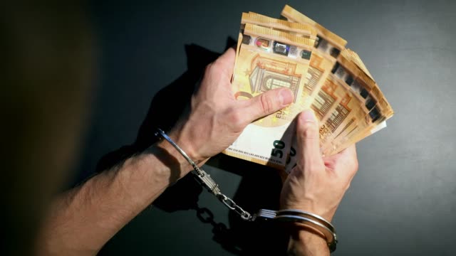 Finanzkriminalität-summiert-sich---Hände-mit-Handschellen-zählen-Euro-Geld