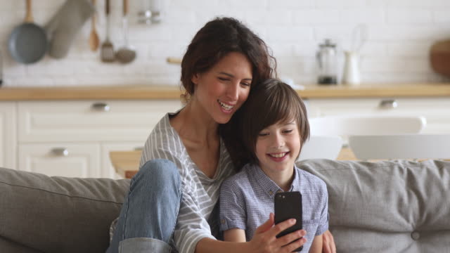 Feliz-madre-e-hijo-de-la-escuela-riendo-usando-el-teléfono-inteligente-en-casa