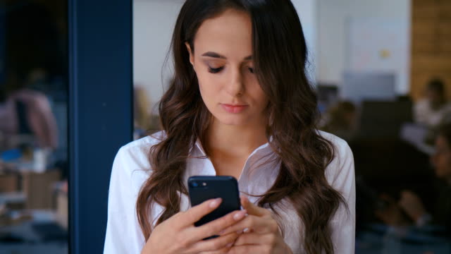 Nahaufnahme-der-schönen-jungen-Geschäftsfrau-mit-Smartphone-SMS-Messenger-im-Büro-im-Hintergrund