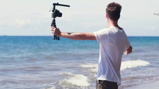 Young-male-vlogger-filming-travel-story-on-the-beach.