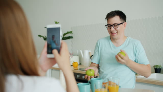 Slow-motion-of-man-juggling-apples-while-woman-taking-photo-with-smartphone
