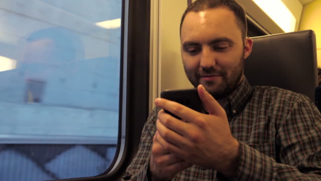 Hombre-guapo-sentado-en-un-tren-subterráneo-y-navegando-en-la-web-con-su-teléfono-inteligente