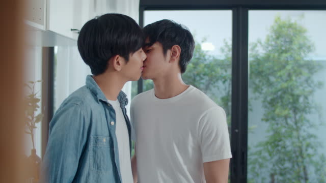 Pareja-gay-asiática-de-pie-y-habitación-de-abrazo-en-casa.-Jóvenes-hombres-LGBTQ+-guapos-besando-feliz-relax-descanso-juntos-pasar-tiempo-romántico-en-la-cocina-moderna-en-casa-en-el-concepto-de-la-mañana.