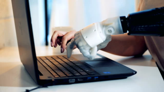 Person-verwendet-Roboterhand,-um-auf-einem-Laptop-zu-tippen,-aus-nächster-Nähe.