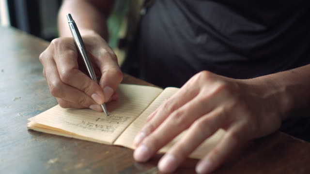 4K-video-copy-space-of-man-hand-writing-down-in-white-notebook-with-bokeh-light-in-cafe-background.
