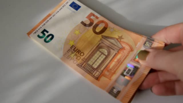 Weibliche-Hand-legt-einen-Haufen-von-fünfzig-Euro-Banknoten-auf-einen-weißen-Tisch,-aus-nächster-Nähe