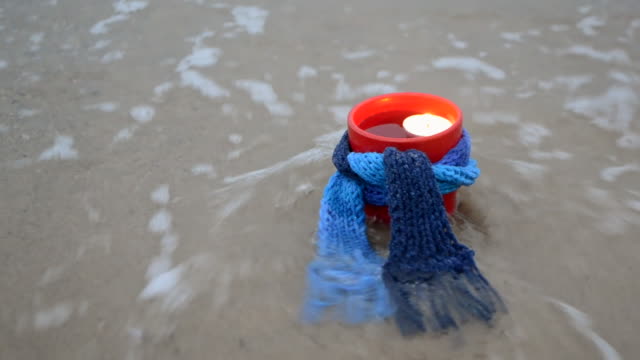 Red-mug-with-coffee-tied-with-blue-knitted-scarf-stands-on-sandy
