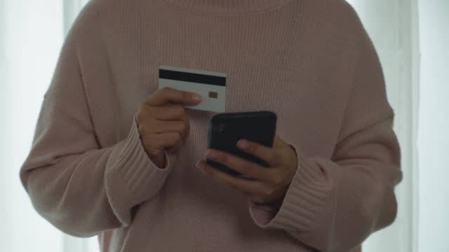 Close-up-hand-of-asian-woman-holding-smartphone-and-credit-card-for-payment-and-shopping-online-at-home.-Happy-woman-making-transaction-using-mobile-bank-application.-Online-shopping-concept.