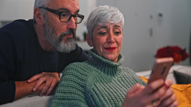 Seniorin-zeigt-Ehemann-Smartphone,-während-sie-auf-dem-Sofa-sitzt