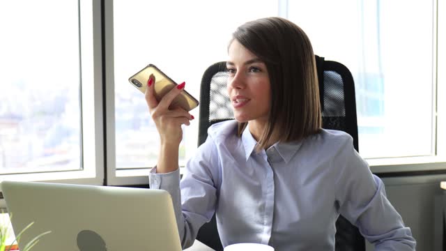 Zuverlässige-Geschäftsfrau-hält-Smartphone-in-der-Nähe-des-Mundes-für-die-Aufzeichnung-von-Sprachnachrichten-oder-die-Aktivierung-digitaler-Assistent.