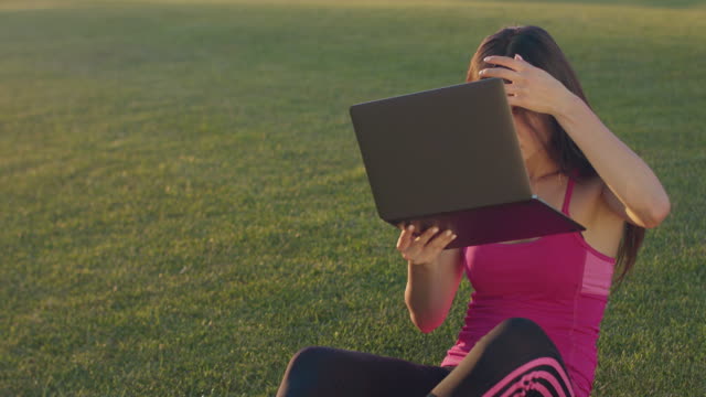 Young-woman-looking-in-laptop-as-in-in-mirror.-Asian-woman-sitting-on-grass