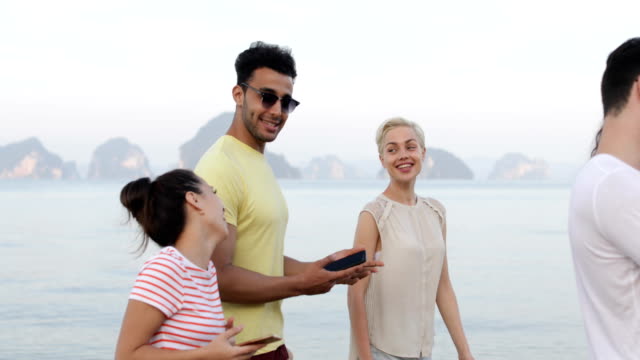 Hablar-usando-celular-inteligente-teléfono-a-pie-de-playa,-jóvenes-turistas-grupo-red-risa-Online