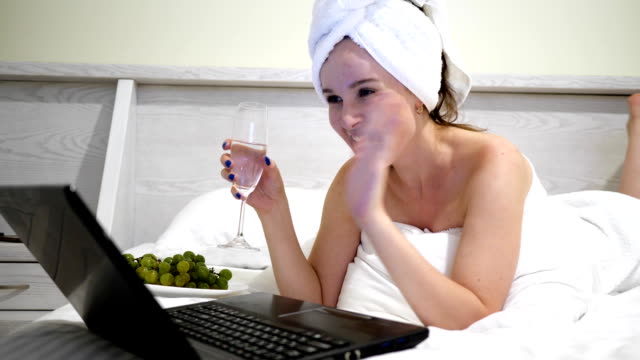 Mädchen-in-Handtuch-auf-Kopf-mit-Champagner-Kommunikation-in-sozialen-Networksto-auf-Laptop-am-Bett