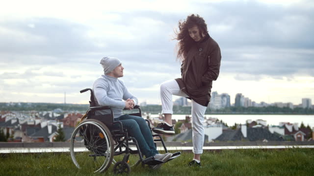Glücklich-behinderte-Menschen-im-Rollstuhl-mit-Frau-im-Gespräch-auf-dem-Hügel