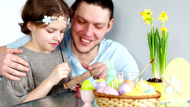Father-and-his-daughter-are-painting-eggs.-Happy-family-preparing-for-Easter.-Cute-little-child-girl-wearing-wreath