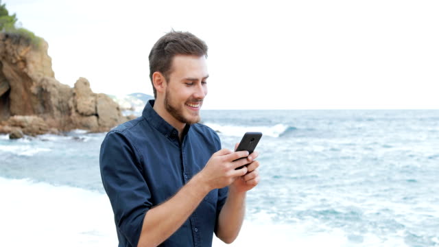 Mann-SMS-auf-Handy-zu-Fuß-am-Strand
