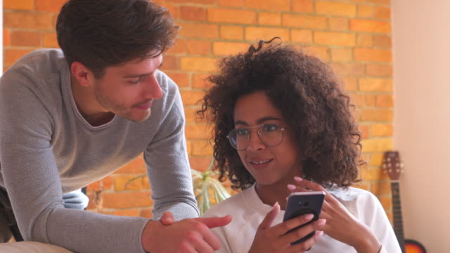 Mixed-race-couple-using-mobile-phone-in-living-room-at-home