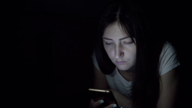 Young-woman-in-the-dark-at-night-sits-with-a-phone-in-social-networks