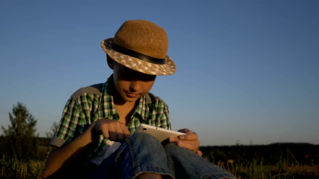 tableta-de-uso-muchacho-sentado-en-el-campo-al-atardecer,-al-aire-libre