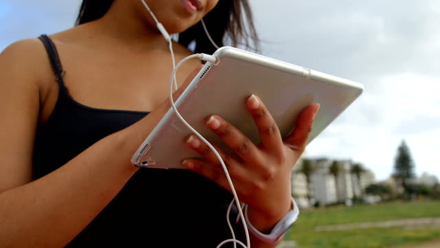 Nahaufnahme-der-behinderte-Frau-Musik-hören-auf-digitale-Tablet-im-Park-4k