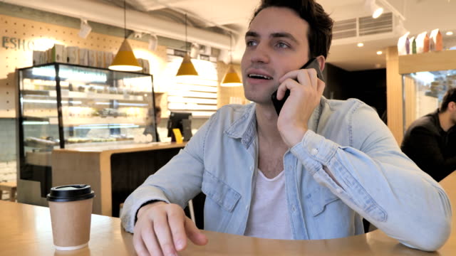 Young-Man-Talking-on-Phone-Sitting-in-Cafe