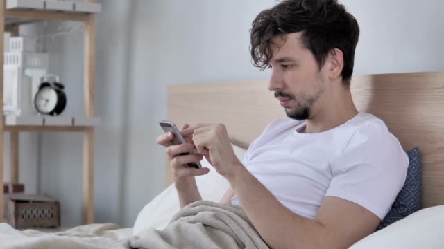 Mann-mittels-Smartphone-beim-liegen-auf-der-Seite-im-Bett