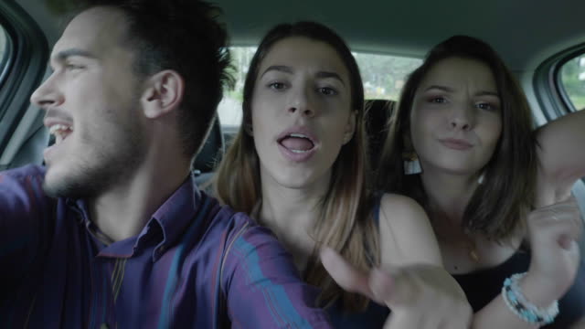 Happy-teenage-man-taking-selfie-video-streaming-with-couple-dancing-funny-crazy-girls-while-they-going-on-summer-holiday-party-and-fun-roadtrip-concept