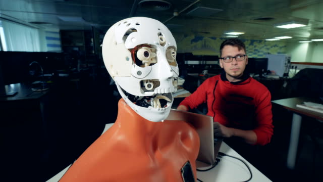 Female-specialist-is-adjusting-a-human-like-mask-on-a-robot's-face