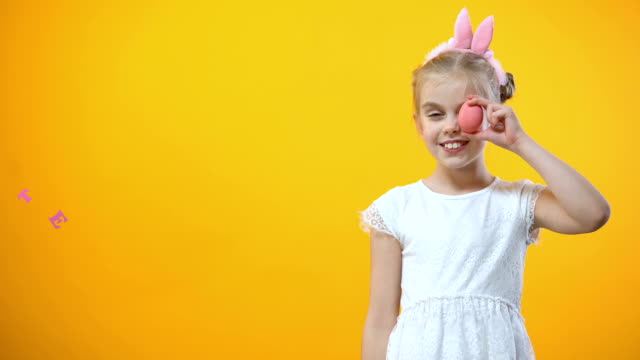 Happy-Easter-inscription,-playful-girl-holding-colored-egg-in-front-of-her-eye