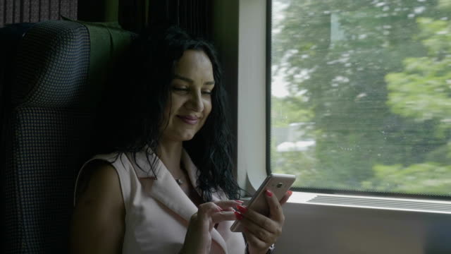 Mujer-joven-con-estilo-conmutando-en-el-tren-sonriendo-mientras-navega-por-Internet-navegando-en-redes-sociales-en-el-teléfono-inteligente