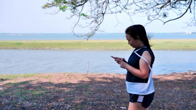 Asiatische-Mädchen-gehen,-trainieren-und-benutzen-das-Telefon-in-der-Natur-mit-der-Sonne-am-Morgen.-Konzept-Gesundheit-mit-Bewegung.-Zeitlupe