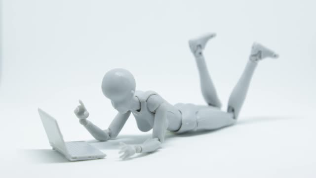 Stop-motion-footage-robot-woman-is-lying-down-and-playing-laptop-on-the-floor-with-white-background.